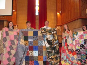 Graduating high school seniors holding up their quilts.